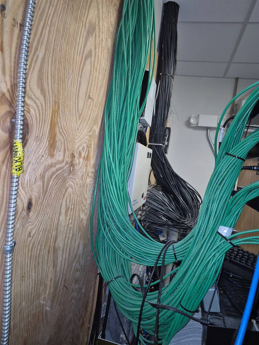 New construction low-voltage rough-in — green Cat6 bundles dropping from ceiling into the telecom closet